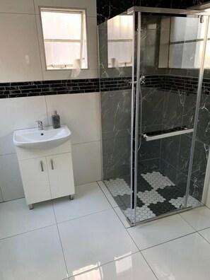 Un baño con un lavamanos blanco, una cabina de ducha con mampara de vidrio y baldosas hexagonales en blanco y negro.