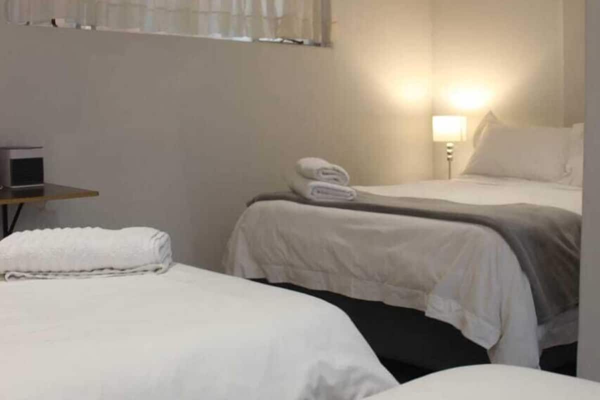 A hotel room with two beds, a bedside table, a lamp, and a window with curtains.