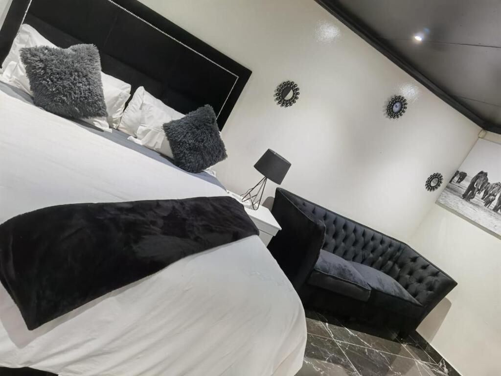 Un dormitorio con una cama, un sofá tapizado negro y una mesita de noche con una lámpara.