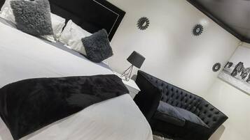 Un dormitorio con una cama, un sofá tapizado negro y una mesita de noche con una lámpara.