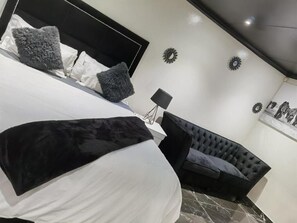 Un dormitorio con una cama, un sofá tapizado negro y una mesita de noche con una lámpara.