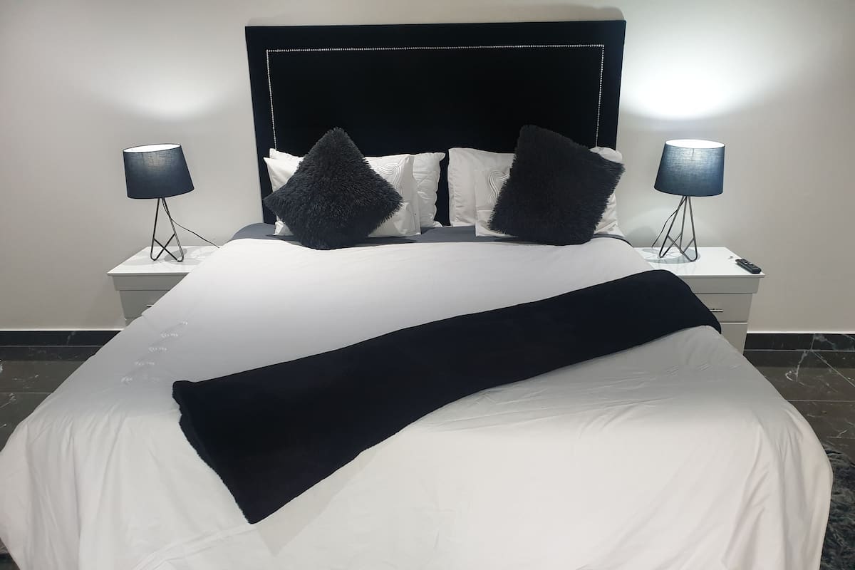 A neatly made bed with a black throw blanket, white bedding, and two black lamps on nightstands.