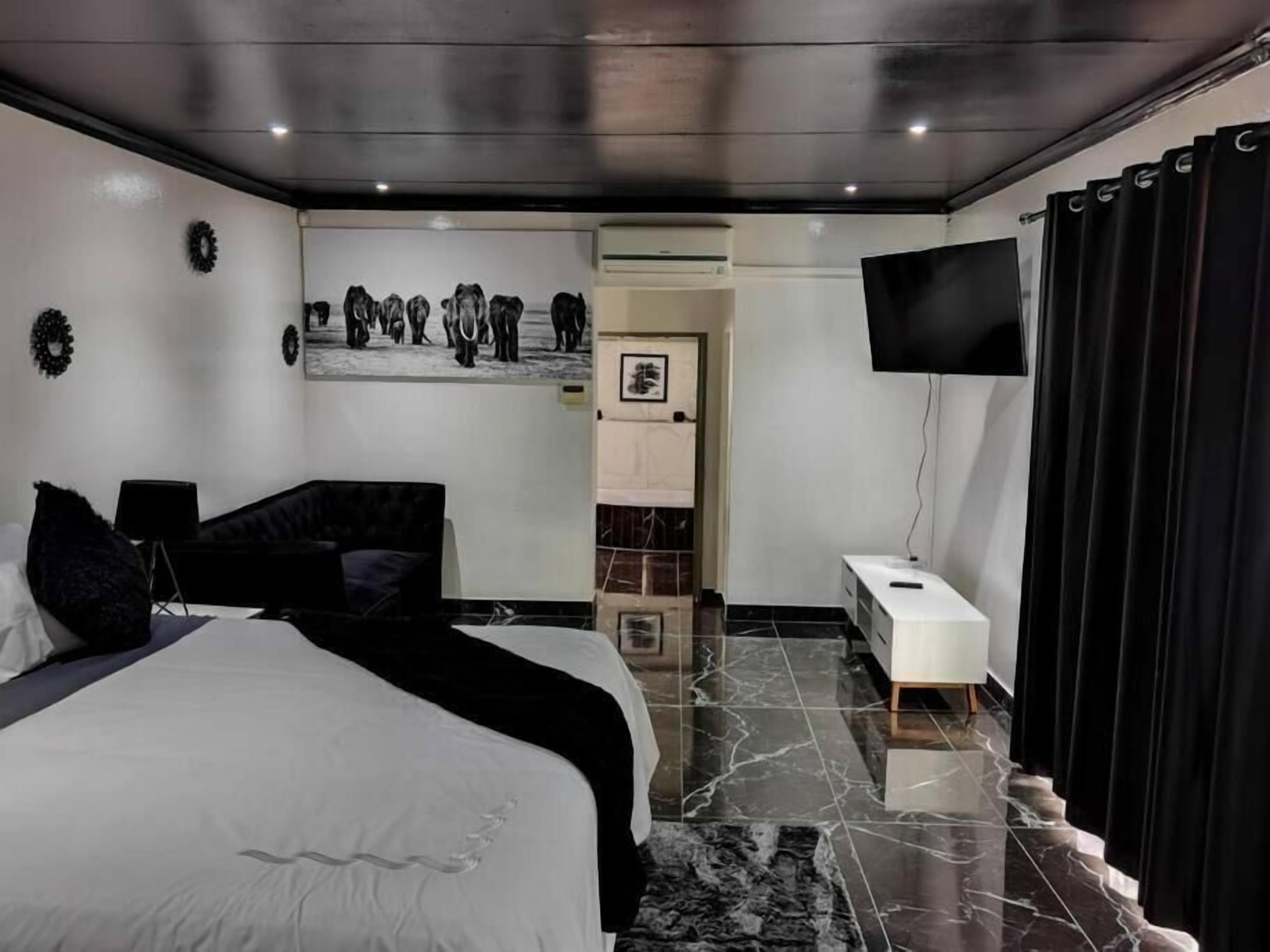 Un dormitorio moderno con una cama grande, un televisor de pantalla plana, una mesita de noche pequeña y suelo de mármol.