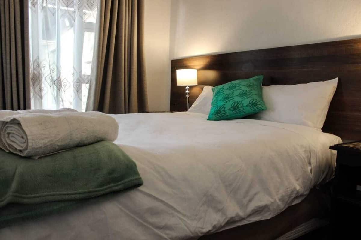A neatly made bed with white linens, a green pillow, and a rolled green towel.