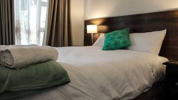 Un lit bien fait, avec des draps blancs, un oreiller vert et une serviette verte enroulée.