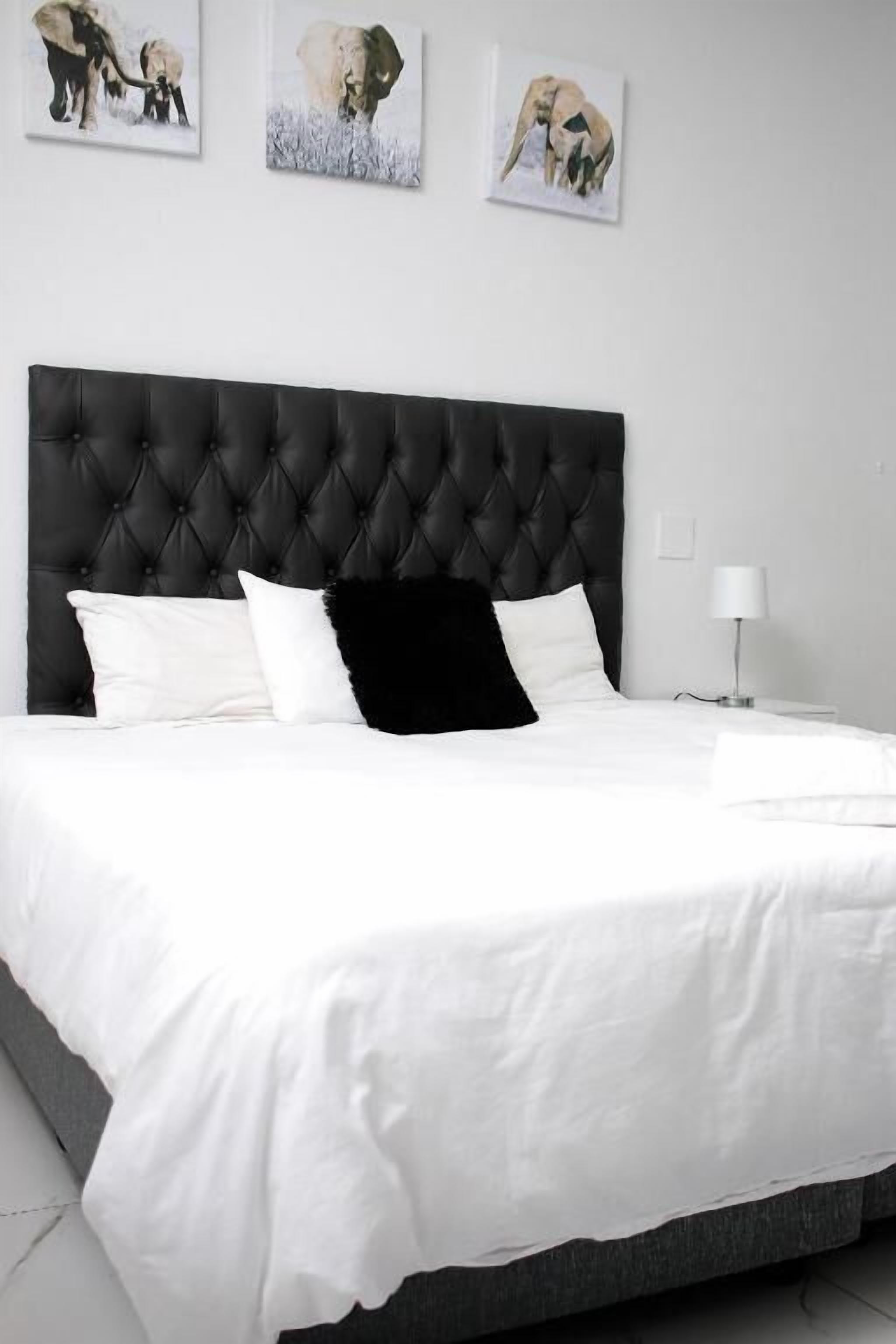 Un dormitorio con cabecera capitonada, ropa de cama blanca y tres cuadros enmarcados en la pared.