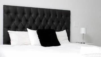 Un dormitorio con cabecera capitonada, ropa de cama blanca y tres cuadros enmarcados en la pared.