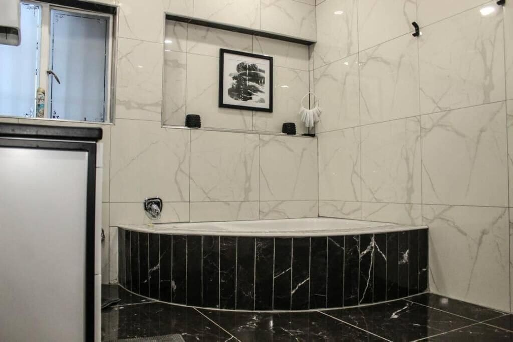 Un baño moderno con una bañera de mármol negro, paredes de mármol blanco y un cuadro enmarcado sobre la bañera.