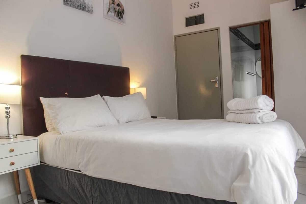 A neatly made bed with white linens, a wooden headboard, and a bedside table with a lamp.
