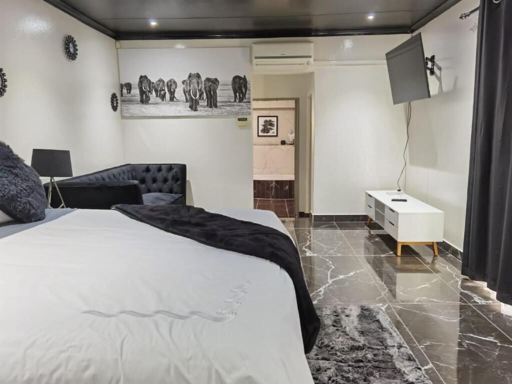 Une chambre à coucher moderne avec un grand lit, un téléviseur à écran plat fixé au mur et un sol en marbre.