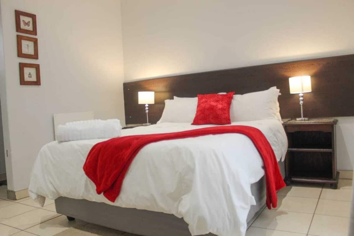 A hotel room with a large bed, white bedding, a red throw blanket, two bedside lamps, and a wooden headboard.