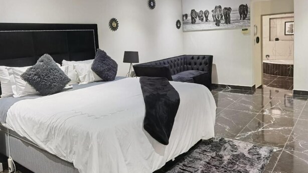 Une chambre à coucher moderne avec un grand lit, une tête de lit sombre et une œuvre d’art représentant des éléphants, accrochée au mur.