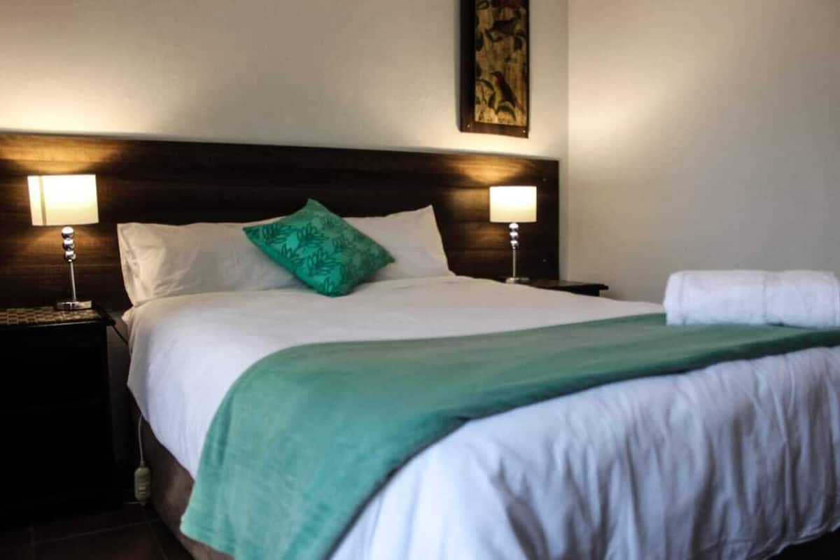 A neatly made bed with white linens and a green throw blanket, flanked by two bedside lamps and a nightstand with a lamp.