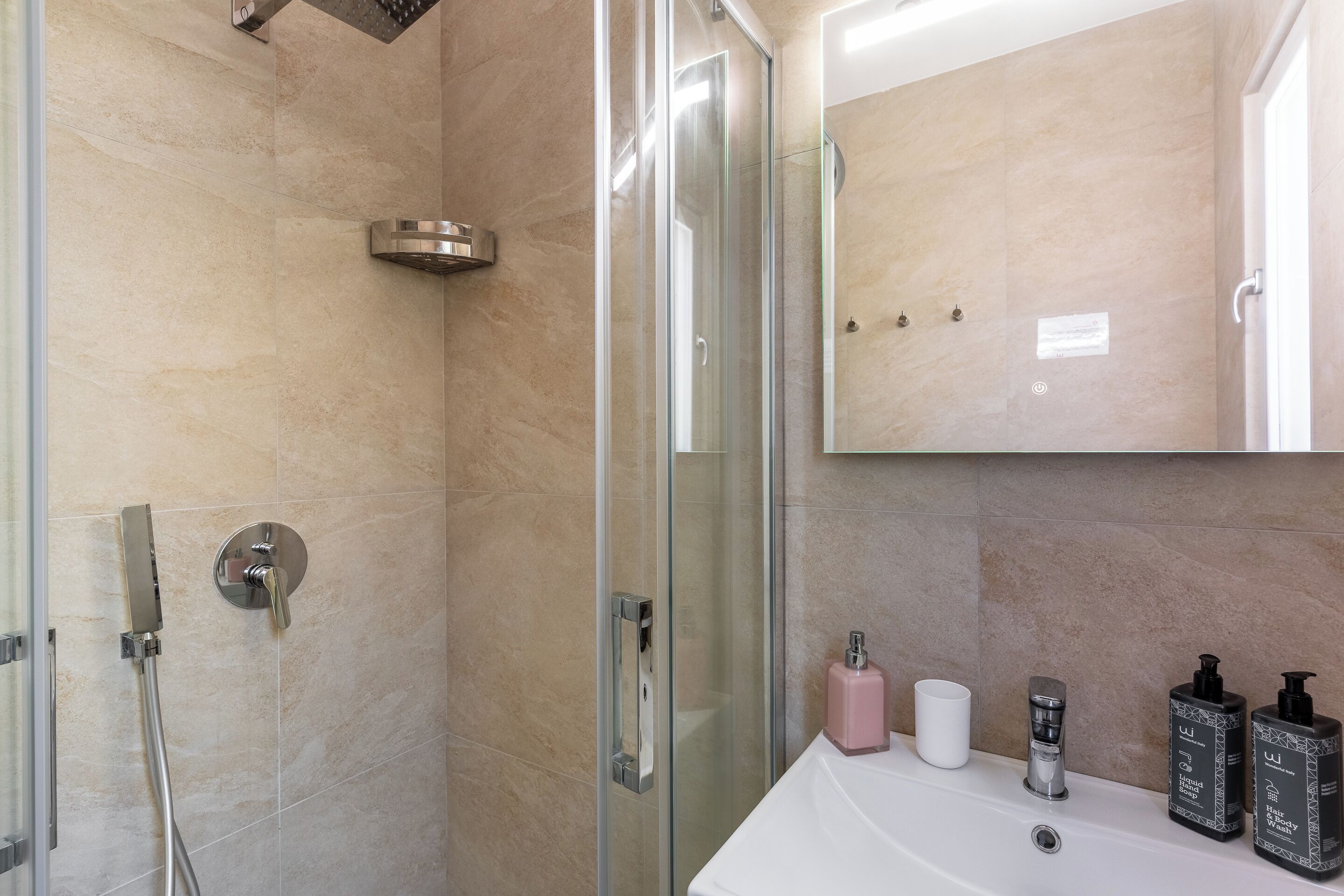 A modern bathroom with a glass shower enclosure, a white sink, and two toiletry bottles.
