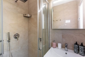 Une salle de bain moderne avec une douche Ă parois de verre, un lavabo blanc et deux flacons de produits de toilette.