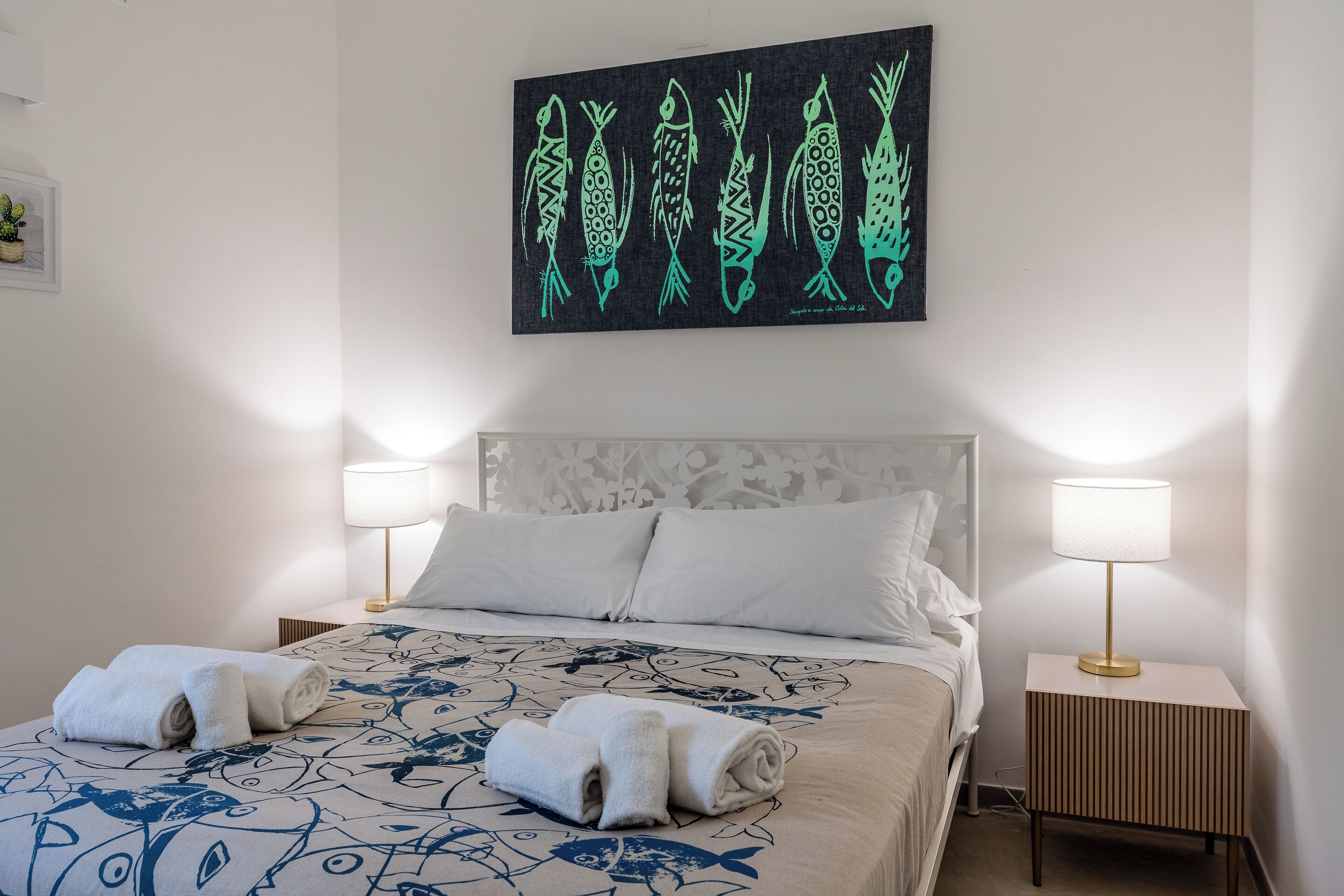 Une chambre d’hôtel avec un lit, deux lampes de chevet, une décoration murale représentant des poissons et un lit soigneusement fait avec des serviettes.