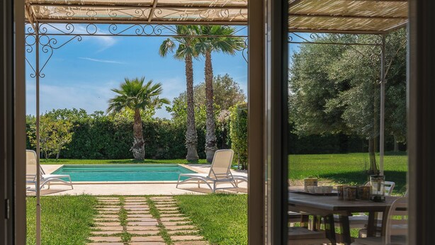 A view of a backyard with a swimming pool, palm trees, and a pergola. - Villa Bouganville by Wonderful Italy (Syracuse)