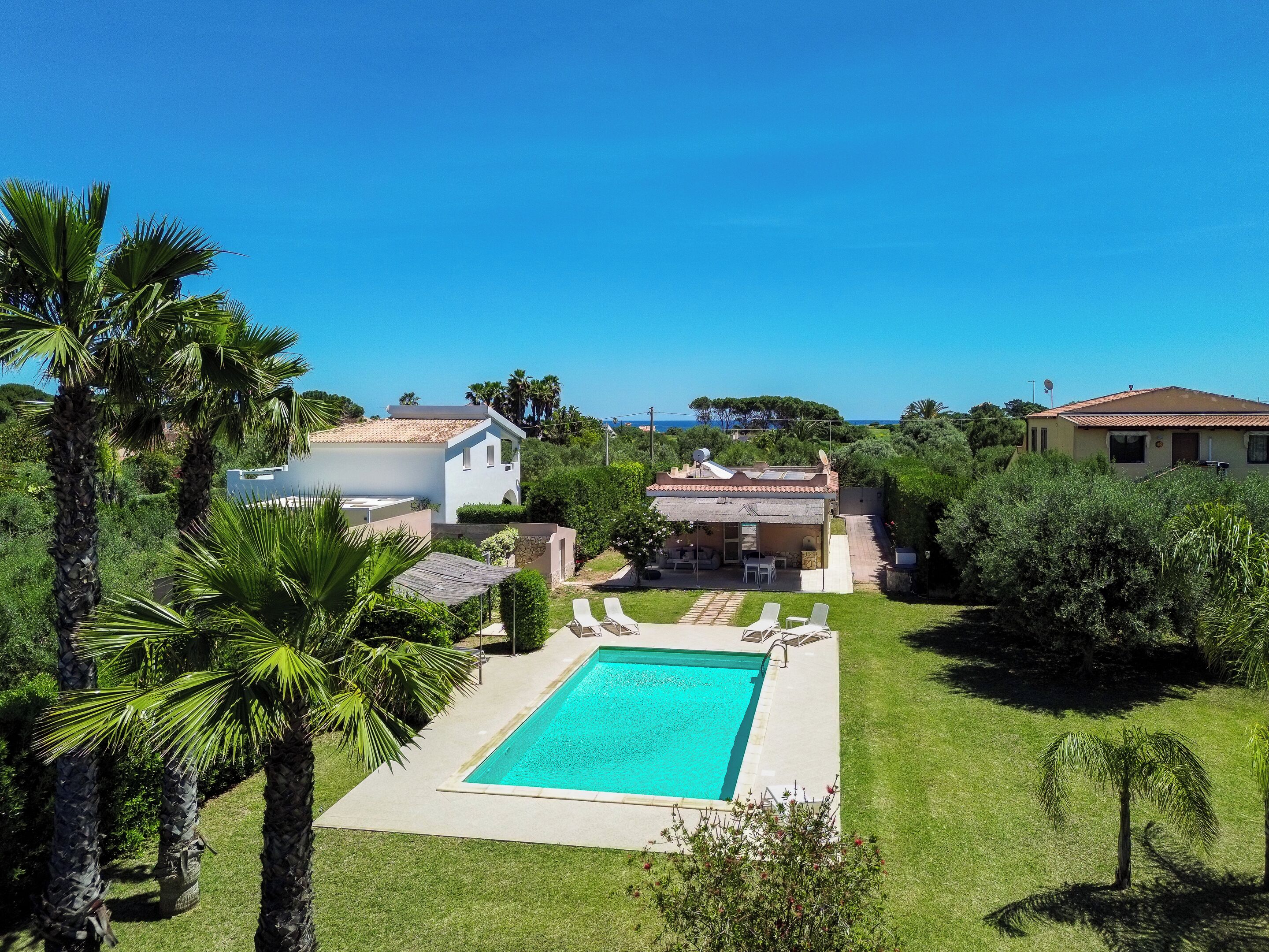 A pool with lounge chairs, a white building, and a red-roofed house.