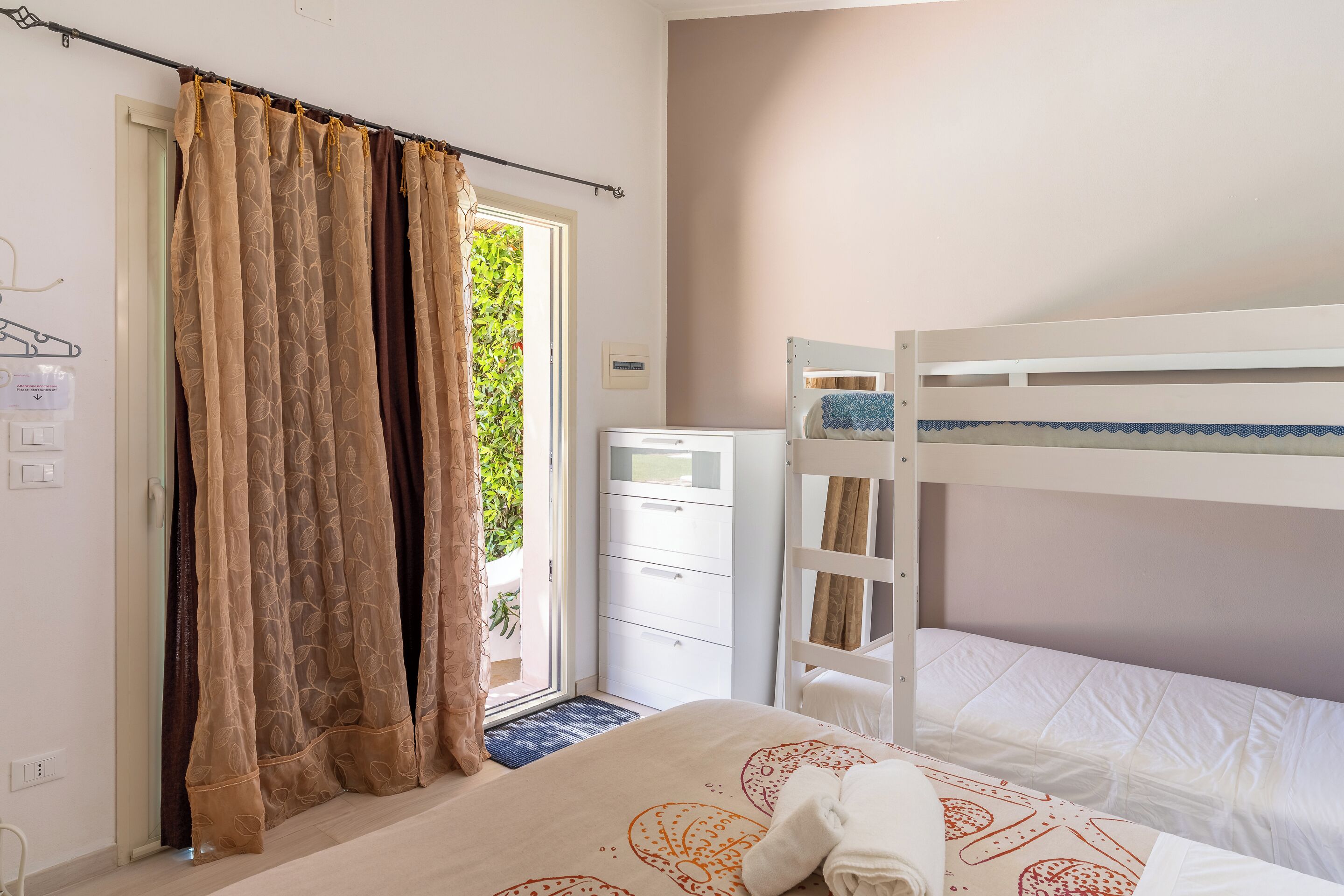 Une chambre avec un lit superposé, une commode blanche et une fenêtre avec des rideaux.