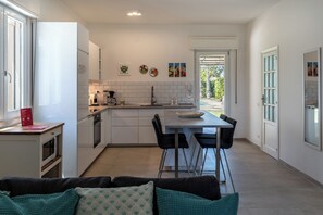 Une cuisine moderne avec des meubles blancs, un coin repas avec des chaises noires et une vue sur l’extérieur.