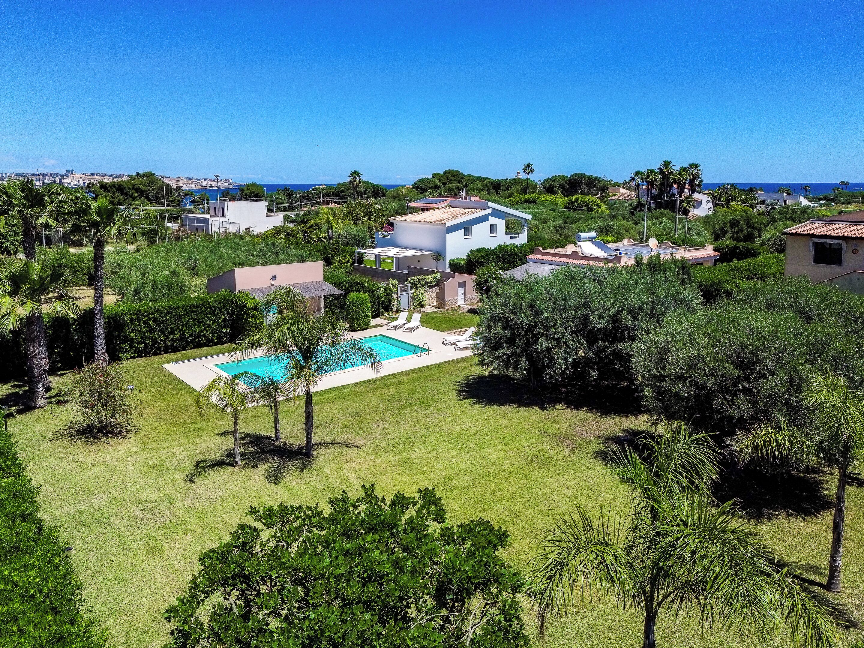 A residential area with a swimming pool, houses, and a view of the sea.
