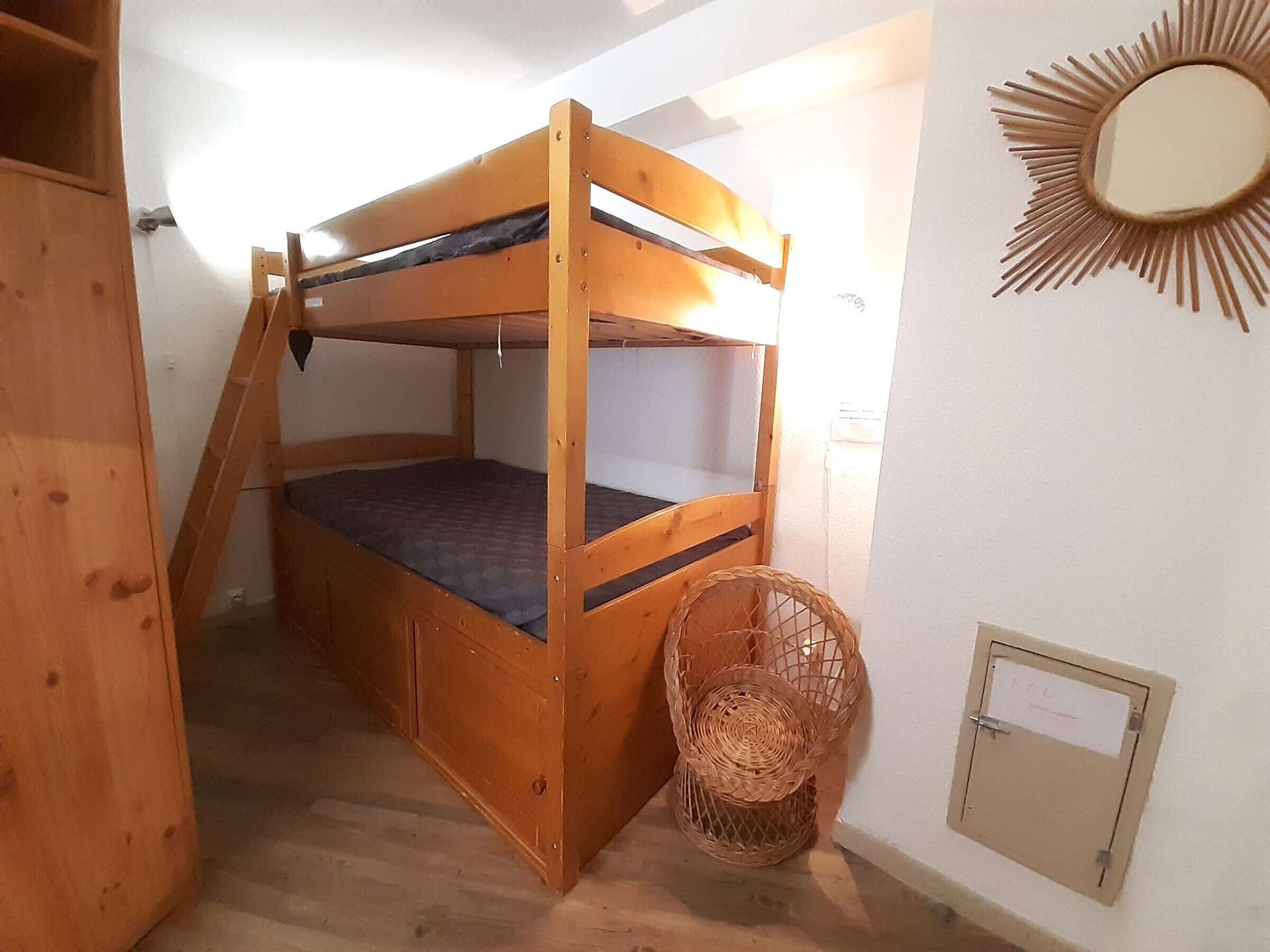 A bunk bed with a ladder, a wicker basket, and a wall-mounted mirror.