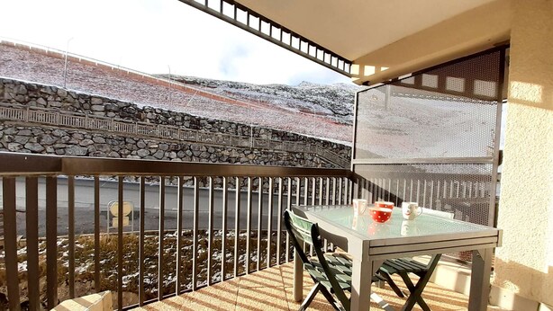Un balcone con tavolo e sedie, un muro in pietra e vista su una strada e montagne.