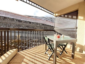A balcony with a table and chairs, a stone wall, and a view of a road and mountains. - T2 6 Pax, balcony, equipped kitchen, ski locker, 1700m, Saint-Lary (Saint-Lary-Soulan)