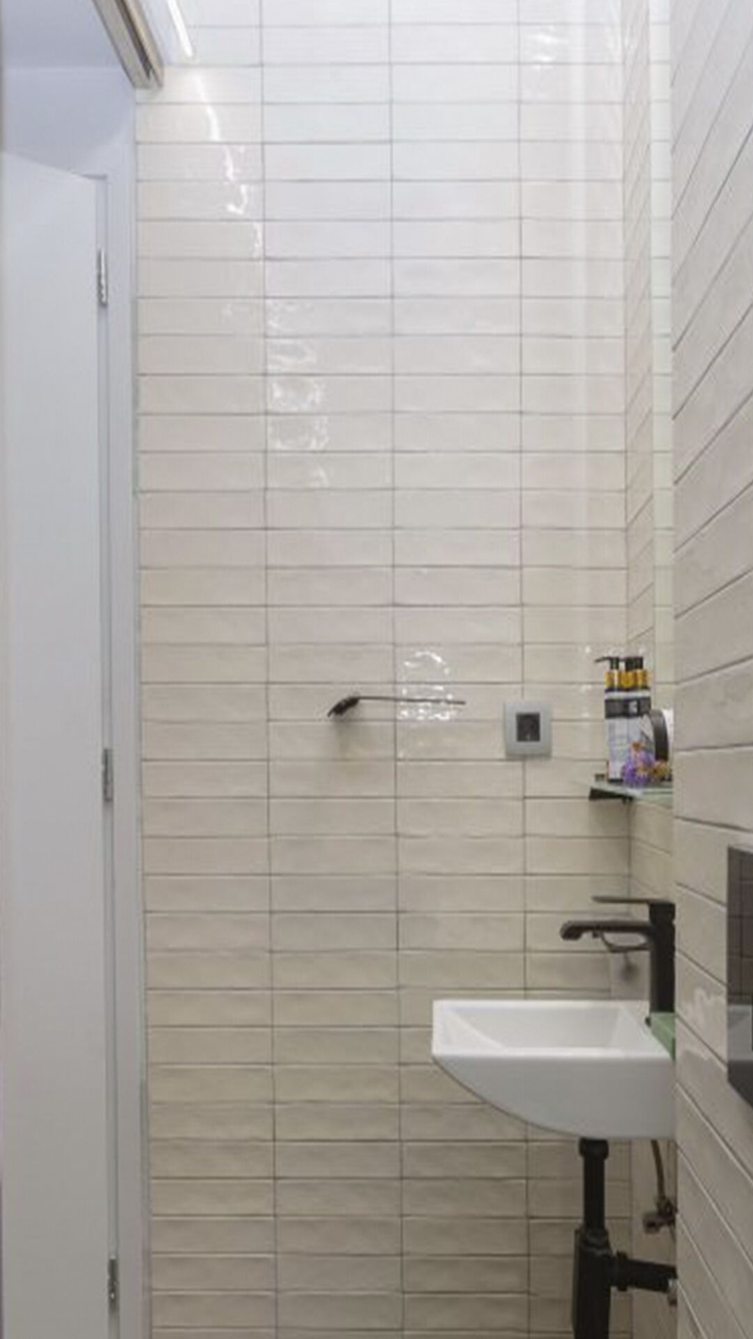 Un baño con paredes de azulejos blancos, un lavamanos blanco y un perchero para toallas.