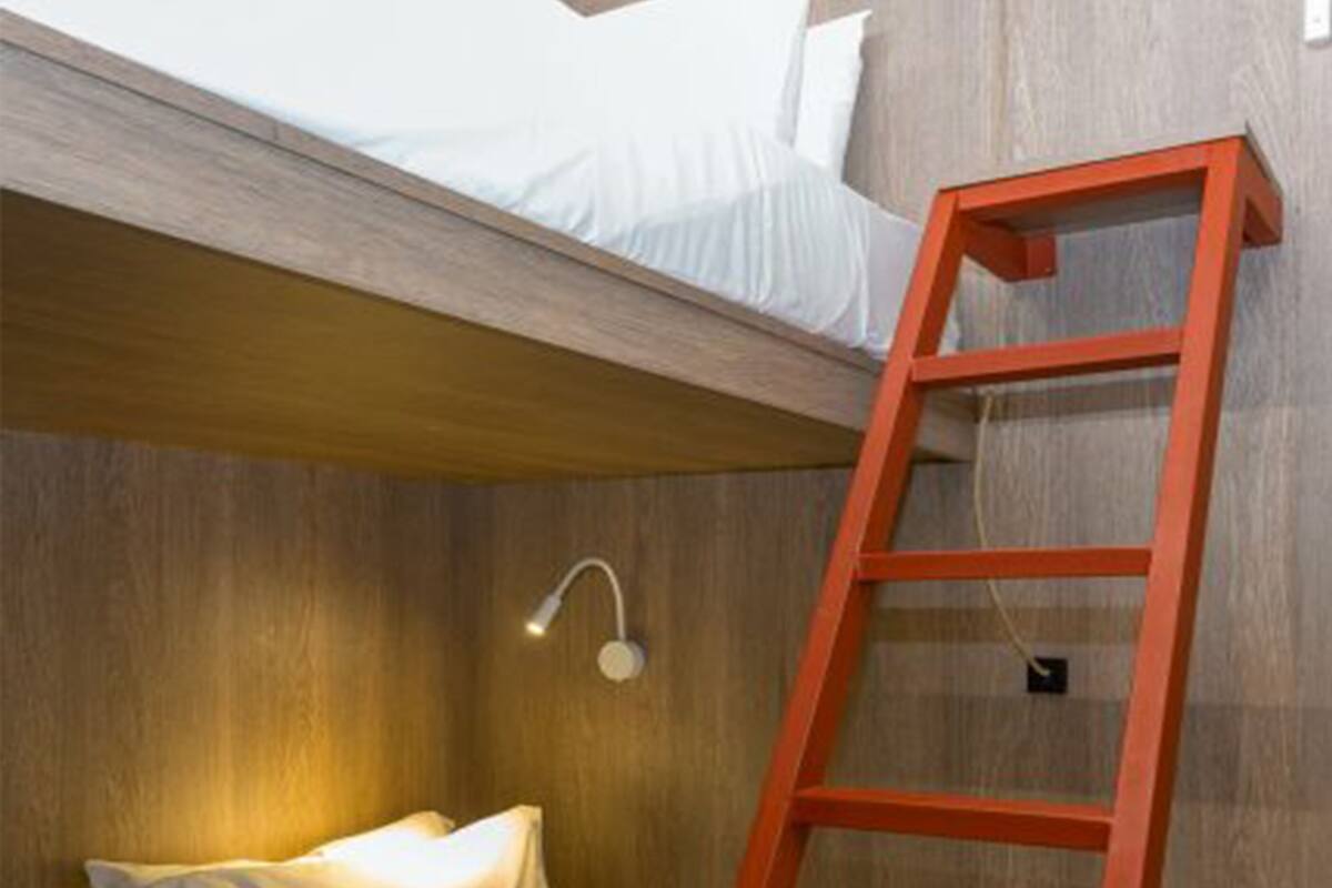 A bunk bed with a ladder, a bedside lamp, and a wooden wall.