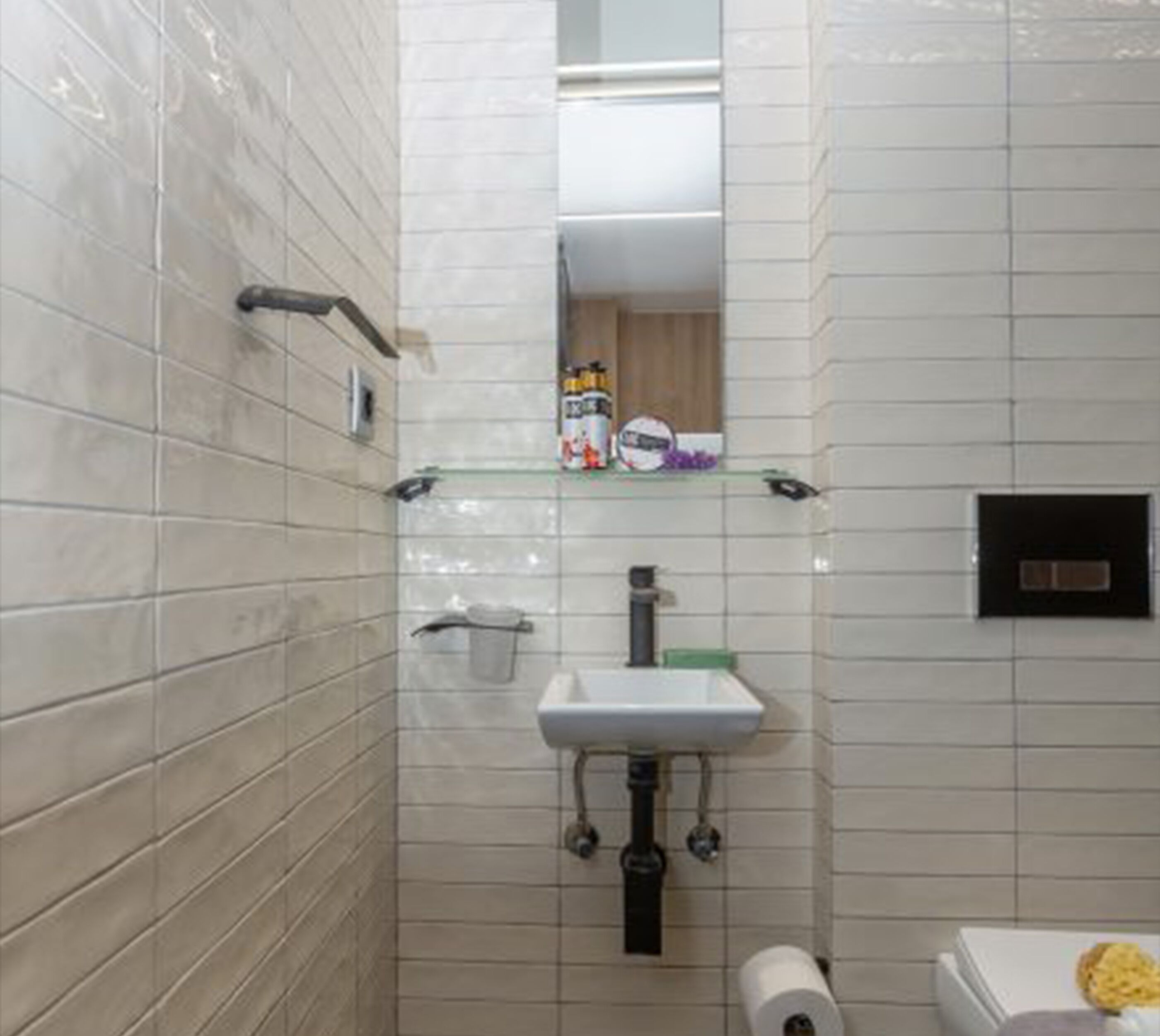 Une petite salle de bain carrelée, avec un lavabo blanc, un miroir et des toilettes.