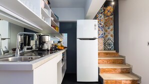 A modern kitchen with a built-in stove, a coffee maker, and a white refrigerator.