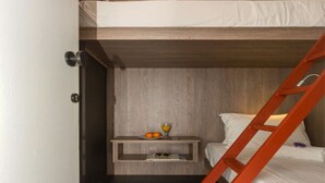 A compact room with a bunk bed, a small bedside table with a glass of orange juice, and a wooden nightstand.
