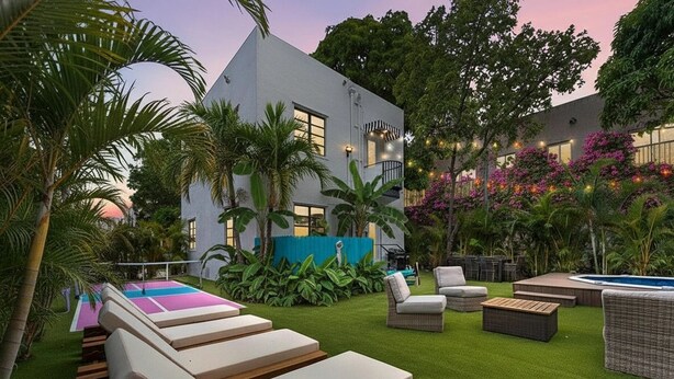 Een moderne buitenlounge met ligbedden, een zwembad en weelderige beplanting.