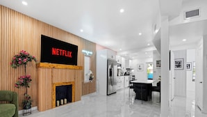 Een moderne woonkamer met een Netflix-bord, een open haard en een groene fauteuil.