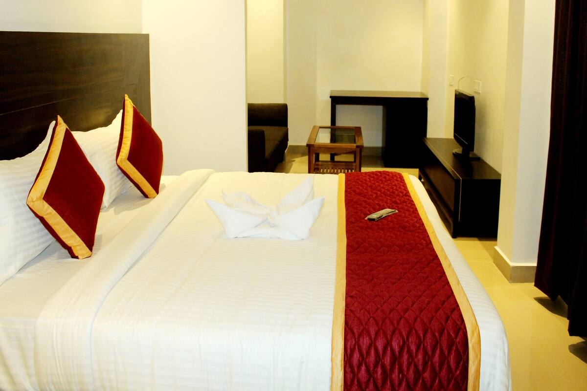 A hotel room with a large bed, a TV, a small table, and a fireplace.