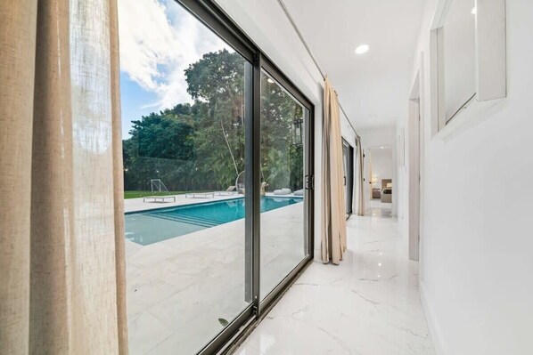 A modern interior with a pool visible through large glass doors. - Luxury Villa Azure with Heated Pool 20min to Beach (Miami)