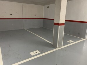 Un aparcament amb places numerades, pilars de formigó i una franja vermella a la paret.