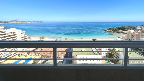 A view from a balcony overlooking a beach with clear blue waters, a distant mountain, and buildings in the background. - Stunning views over the sea + parking. TOP (Calpe)