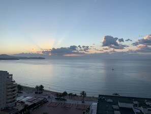 Vista costanera amb un mar tranquil, una illa a la distància i un hotel amb terrassa al terrat.