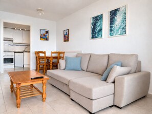Un salon moderne avec un canapé beige, une table à manger en bois et des chaises. On y trouve également un coin cuisine avec des meubles blancs et une cuisinière.