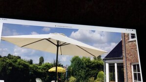 Une terrasse extérieure avec une table et des chaises, un grand parasol et un mur de briques en arrière-plan.