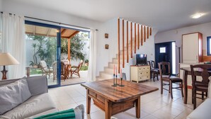En moderne stue med sofa, sofabord og spiseplads. Der er en trappe til et andet niveau, og et fjernsyn på et skab.