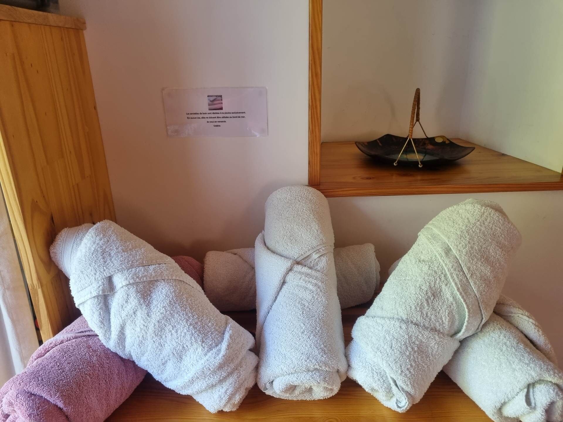 A wooden shelf with folded towels in white and pink, a small sign, and a decorative item.