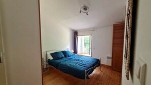 Un dormitorio con cama, suelo de madera, ventana con cortinas y ventilador de techo.