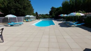 Una piscina con suelo de baldosas, rodeada de sillas de descanso y sombrillas.