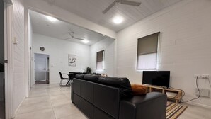 A modern living room with a black sofa, a dining area with a table and chairs, a TV, and a ceiling fan.