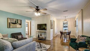 Ein Wohnzimmer mit einer Couch, einem Fernseher, einem Deckenventilator und einem Essbereich mit Tisch und Stühlen.
