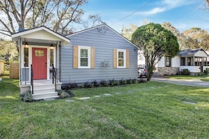 A single-story house with a front porch, a red door, and a small front yard.