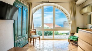A room with a large arched window, a wooden chair, a small table, and a green sofa. - Villa Marghe - Sea View Rooms (Massa Lubrense)